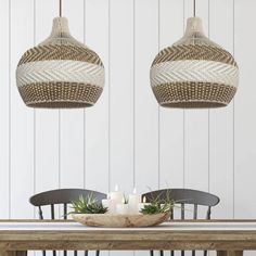 two wicker lamps hanging over a dining room table with candles and succulents