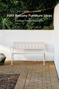 a white bench sitting on top of a brick floor next to a wall and trees