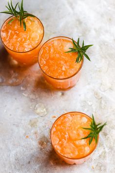 three small glasses filled with orange juice and garnished with green sprigs