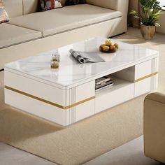 a white coffee table with gold trim around the edges and drawers in front of a beige couch