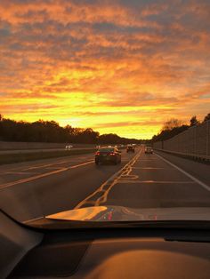 cars driving down the highway at sunset with clouds in the sky and trees on either side