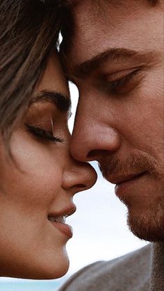 a man and woman kissing each other with their foreheads close to one another as they look into the distance