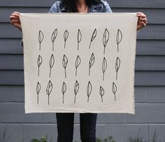 a woman holding up a black and white print with leaves on it in front of a gray wall