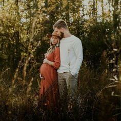 a pregnant couple is standing in tall grass