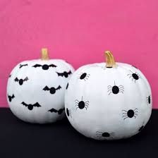 two white pumpkins with bats painted on them sitting side by side against a pink wall