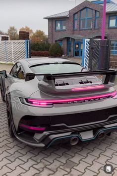 a grey sports car parked in front of a house with pink lights on the hood