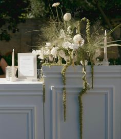 a vase with flowers and candles sitting on top of a white cabinet next to a sign