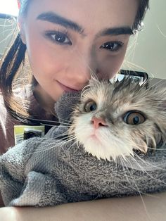 a woman is holding a cat wrapped in a towel and posing for the camera with her eyes wide open