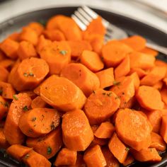 a plate full of sliced carrots with a fork in the bowl next to it