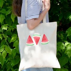 a woman carrying a watermelon tote bag in front of some bushes and trees