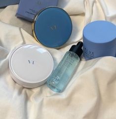 various skin care products are laying on a white sheet with a blue box next to it