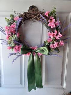 a wreath with pink flowers and green ribbon hanging on the front door, next to a bird's nest