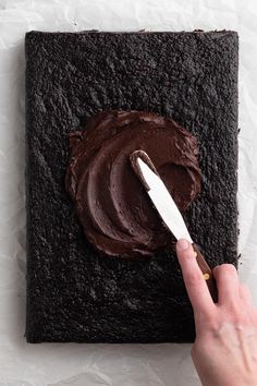 a person is spreading chocolate frosting on a square piece of brownie with a knife