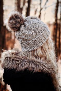 a woman wearing a knitted hat with a fur pom - pom in the woods