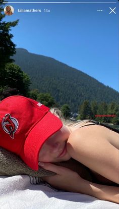 a woman wearing a red hat laying on top of a white blanket next to a forest