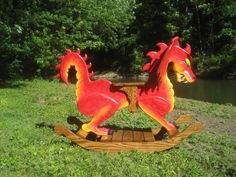 a red and yellow horse on a wooden sleigh in the grass next to water