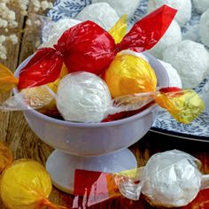 two bowls filled with assorted candies on top of a wooden table next to plates