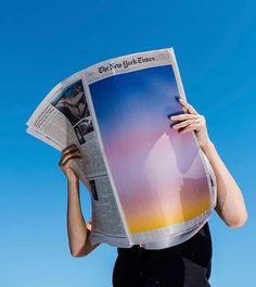 a woman holding up a newspaper with the sky in the background