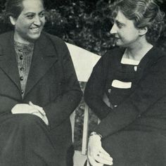 two women sitting next to each other in black and white photo with trees behind them