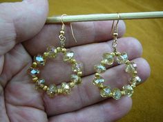 a hand holding a pair of gold colored beaded hoop earrings with clear crystal beads