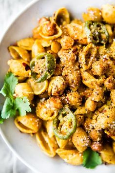 a white bowl filled with pasta covered in pesto sauce and topped with parsley