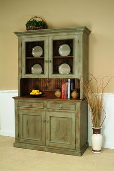 an old green china cabinet with plates on top and two vases next to it