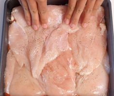 two hands on top of raw chicken in a pan