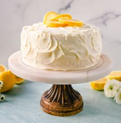 a cake with white frosting and orange slices sitting on a plate next to flowers