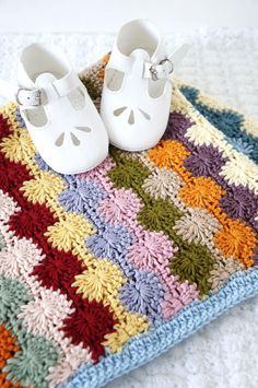 a pair of baby shoes sitting on top of a crocheted blanket