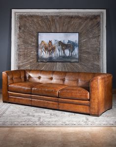 a brown leather couch sitting in front of a painting