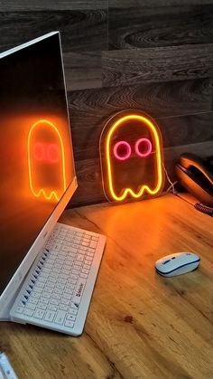 a laptop computer sitting on top of a wooden desk next to a neon ghost sign