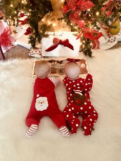 two baby dolls laying next to each other in front of a christmas tree with presents