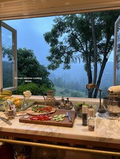 a kitchen counter with food on it in front of an open window overlooking the trees