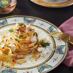 a plate topped with pasta and vegetables on top of a table next to wine glasses