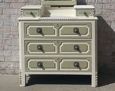 an old dresser with a mirror on top and drawers below it, sitting in front of a brick wall