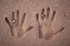 two hand prints in the sand with rings on them