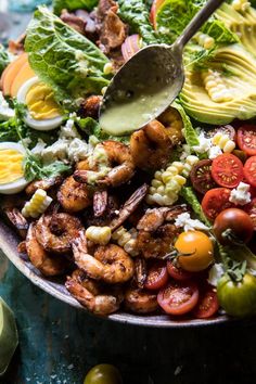 a salad with shrimp, tomatoes, avocado, corn and dressing on it