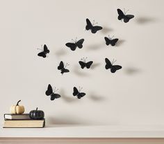 there are many black butterflies flying in the air above books and pumpkins on top of a table