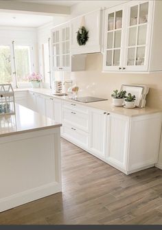 a large kitchen with white cabinets and wood flooring, along with an island in the middle