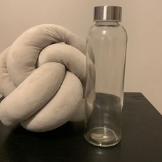 a glass bottle with a white pillow next to it on a black table near a large round object