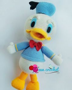 a crocheted stuffed duck wearing a blue dress and red bow tie, standing on a white background