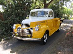 an old yellow truck is parked on the side of the road in front of some trees