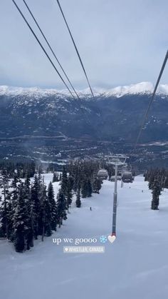 a ski lift going up the side of a snow covered mountain with trees and mountains in the background