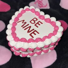 a pink and white cake sitting on top of a black table covered in heart shapes