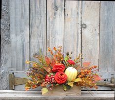 an arrangement of flowers and leaves sits on a bench