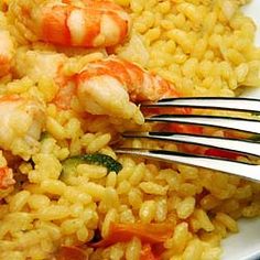 a white plate topped with rice and shrimp next to a fork on top of it