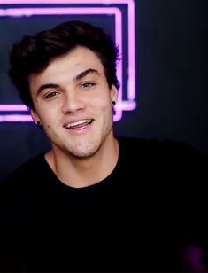 a young man is smiling in front of a neon sign that reads, i love you