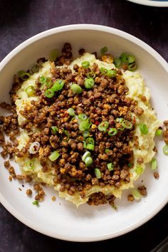 a white bowl filled with mashed potatoes topped with ground meat and green onions on top