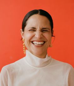 a smiling woman wearing gold earrings and a white shirt