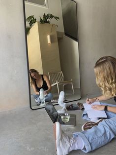 a woman sitting on the floor in front of a mirror with her legs crossed and writing